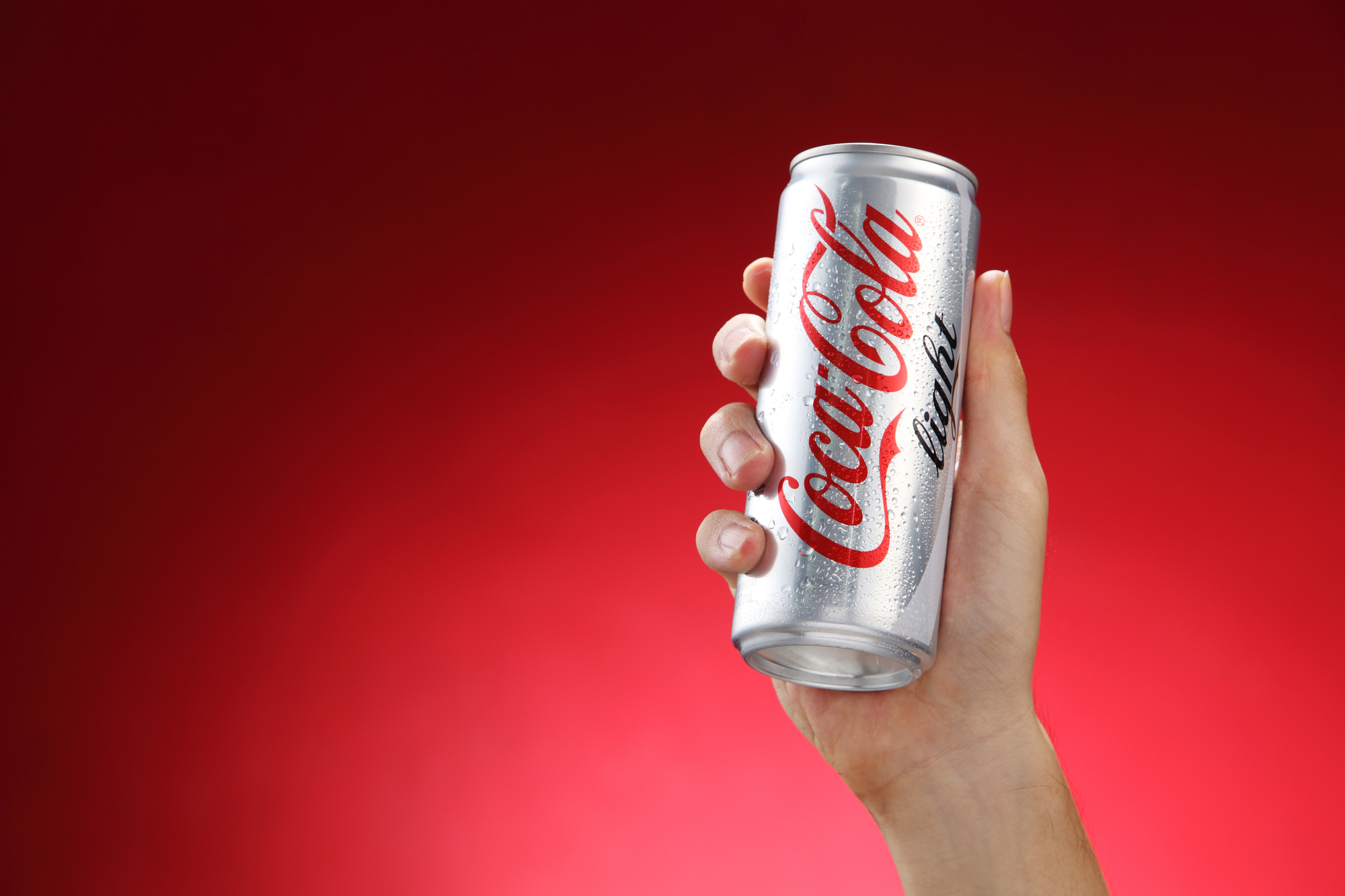 Kuala Lumpur,Malaysia 11th July 2016, Hand hold a can Coca-Cola light on red background. Coca Cola drinks are produced and manufactured by The Coca-Cola Company.